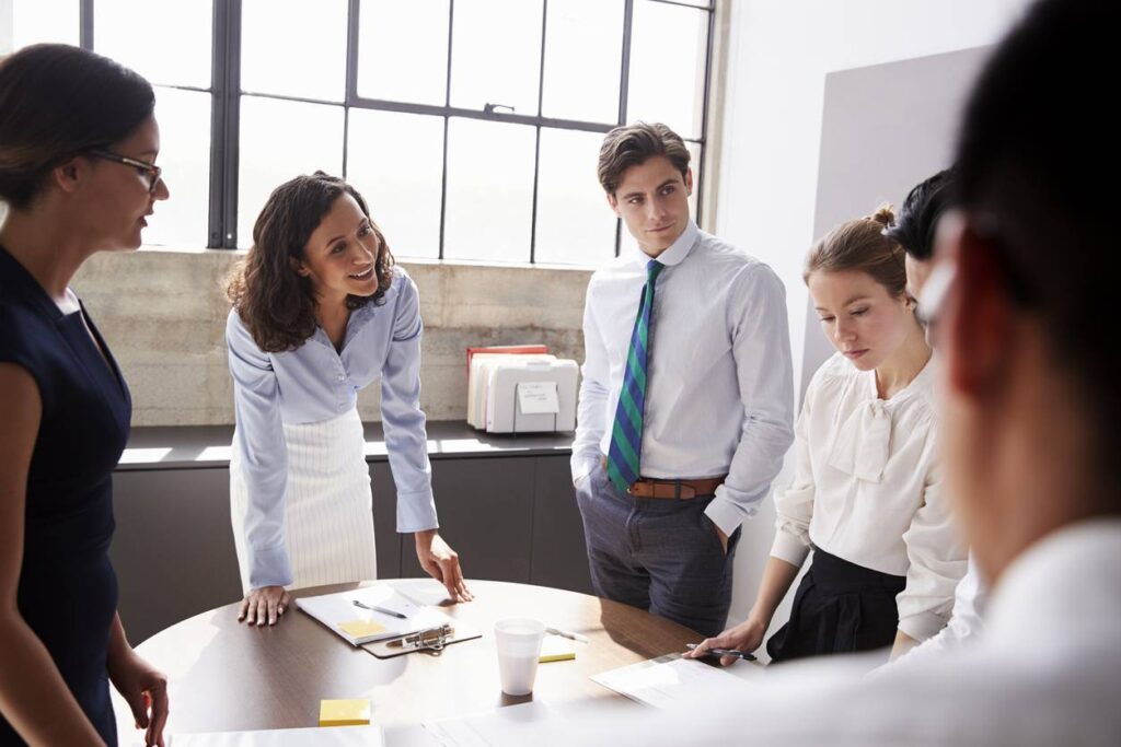 A group of people standing around a table for a nonprofit board member meeting