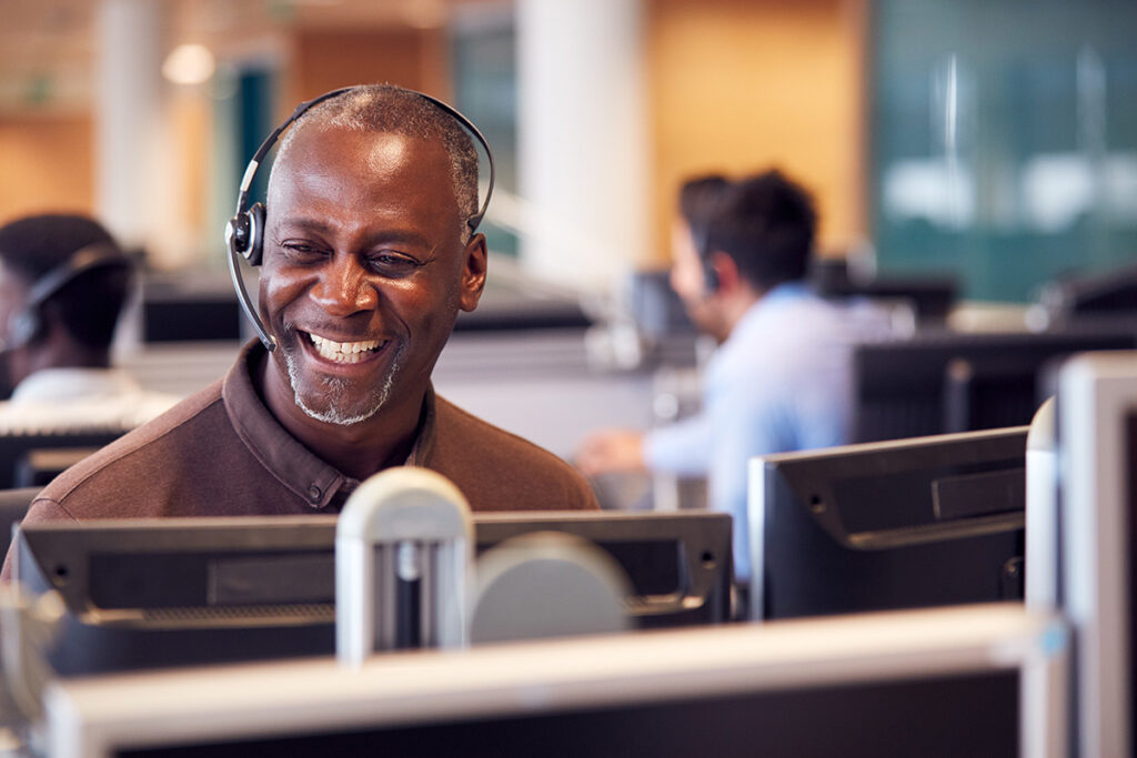 man seen smiling as he is sitting in an office with a headset on