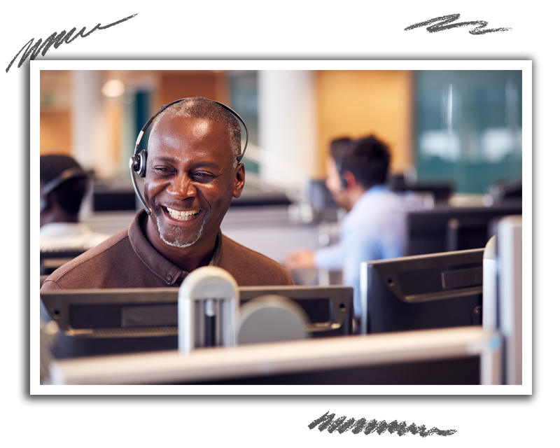 man seen smiling as he is sitting in an office with a headset on