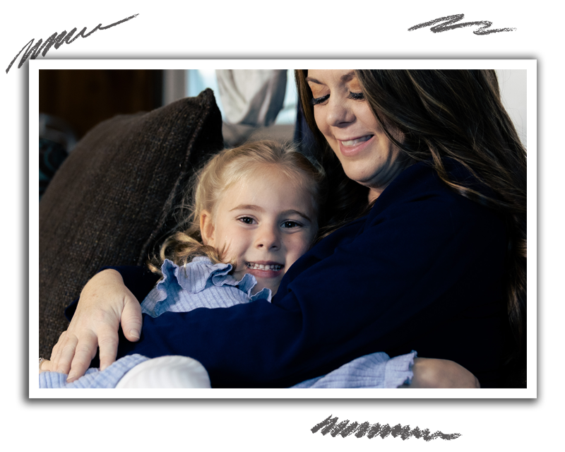 a young girl smiling as she is wrapped up in an embrace by a woman