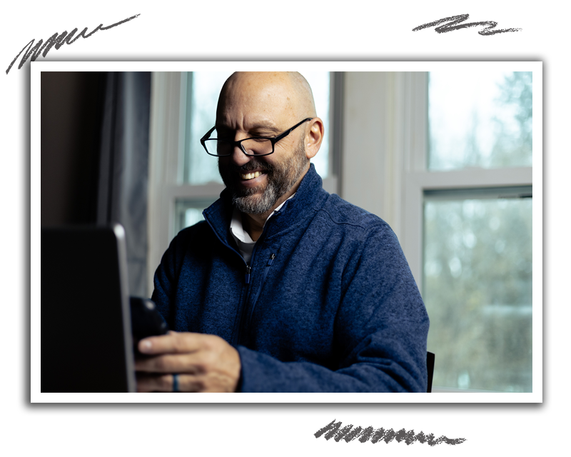 man smiling while working on his phone and laptop