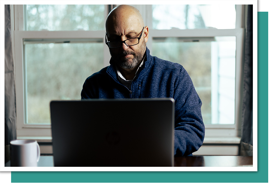 a man sitting, working on a laptop with a window with a scenic view behind him