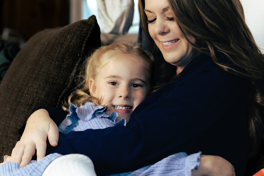 a young girl smiling as she is wrapped up in an embrace by a woman