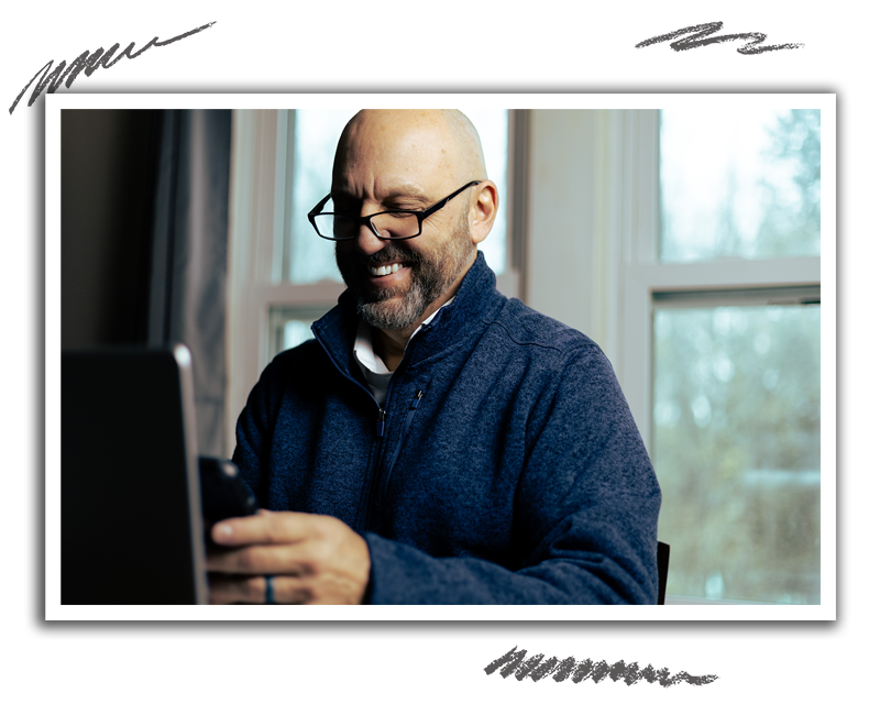 man smiling while working on his phone and laptop