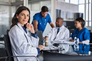 doctor sitting confidently at a boardroom while doctors and nurses discuss in the background