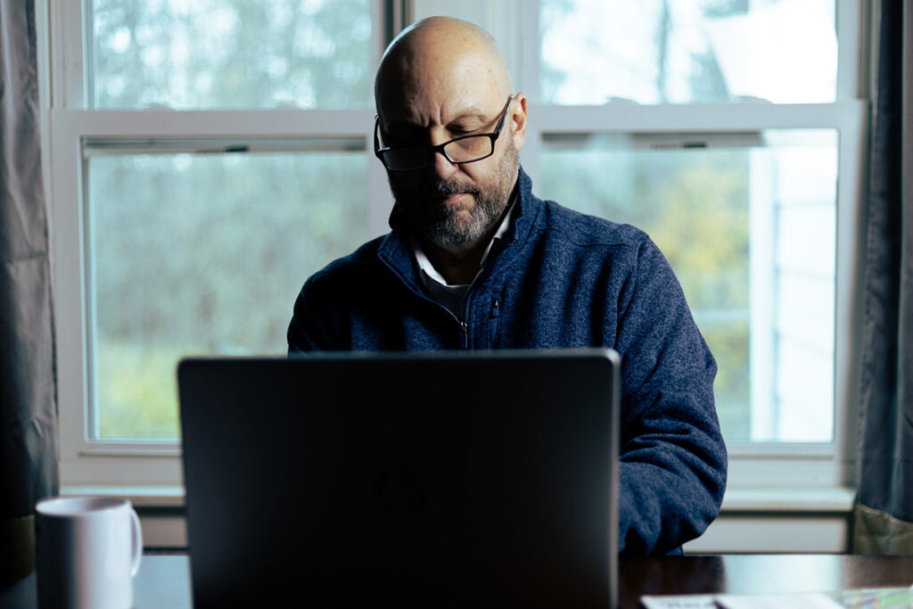 CFO sitting at a private, home office working on a laptop while enjoying a cup of coffee